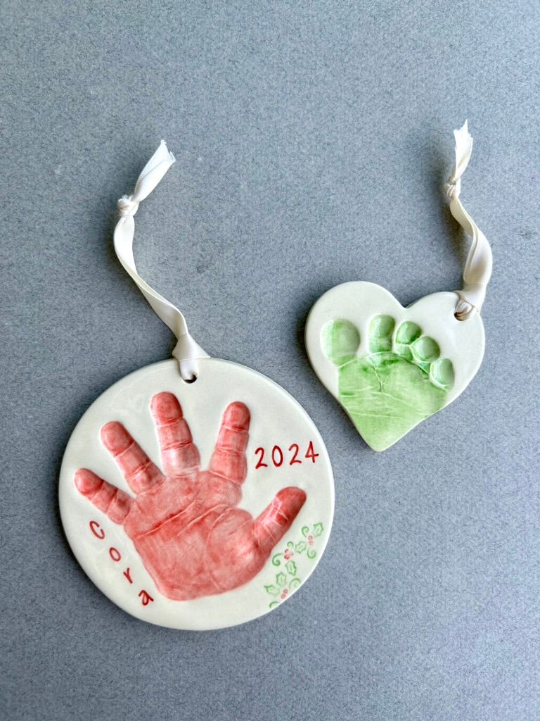 Red handprint and green footprint heart ceramic ornaments, dated 2024.