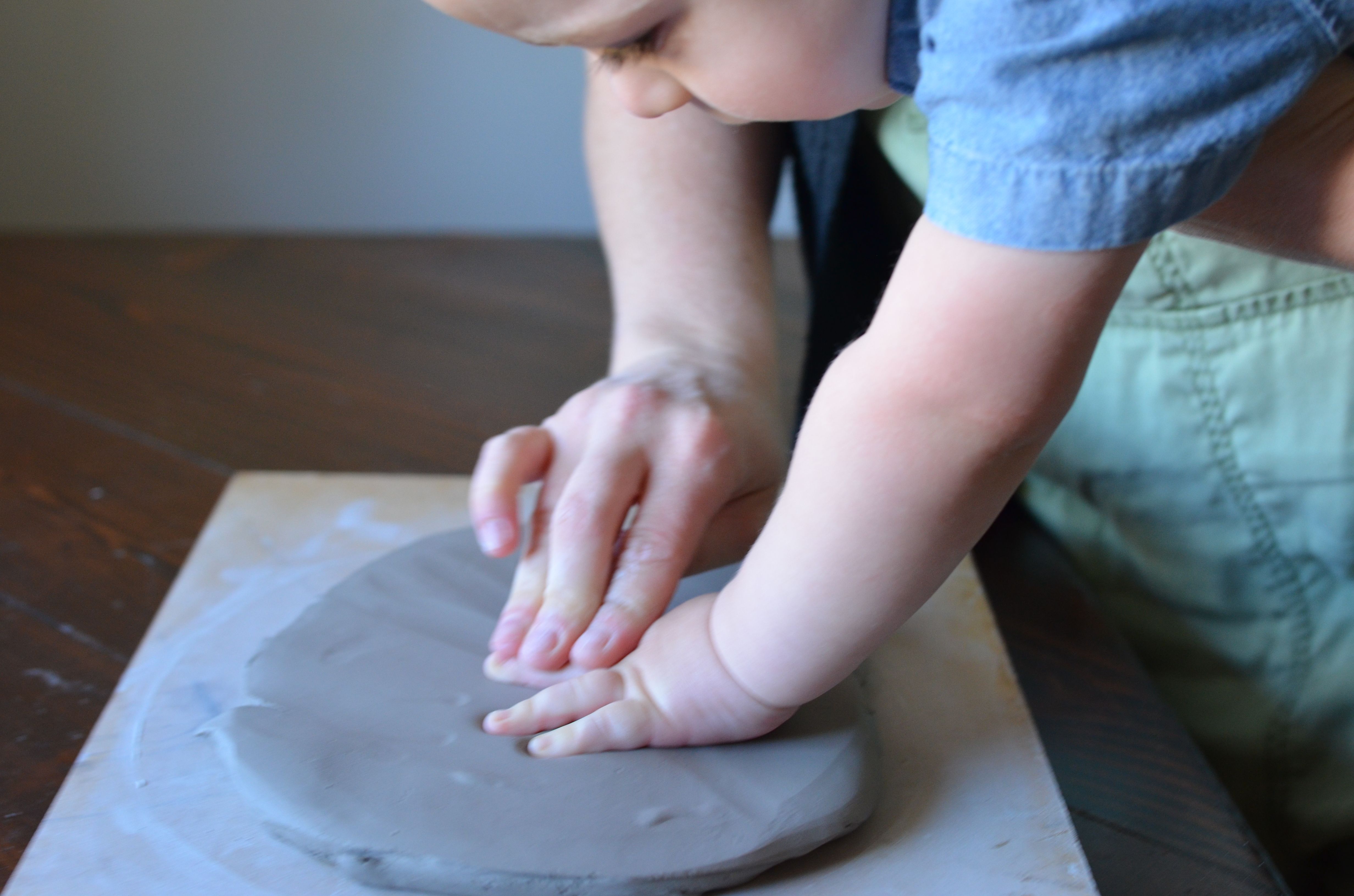 A toddler pressing their hand into a smooth clay slab with a grown-up guiding.