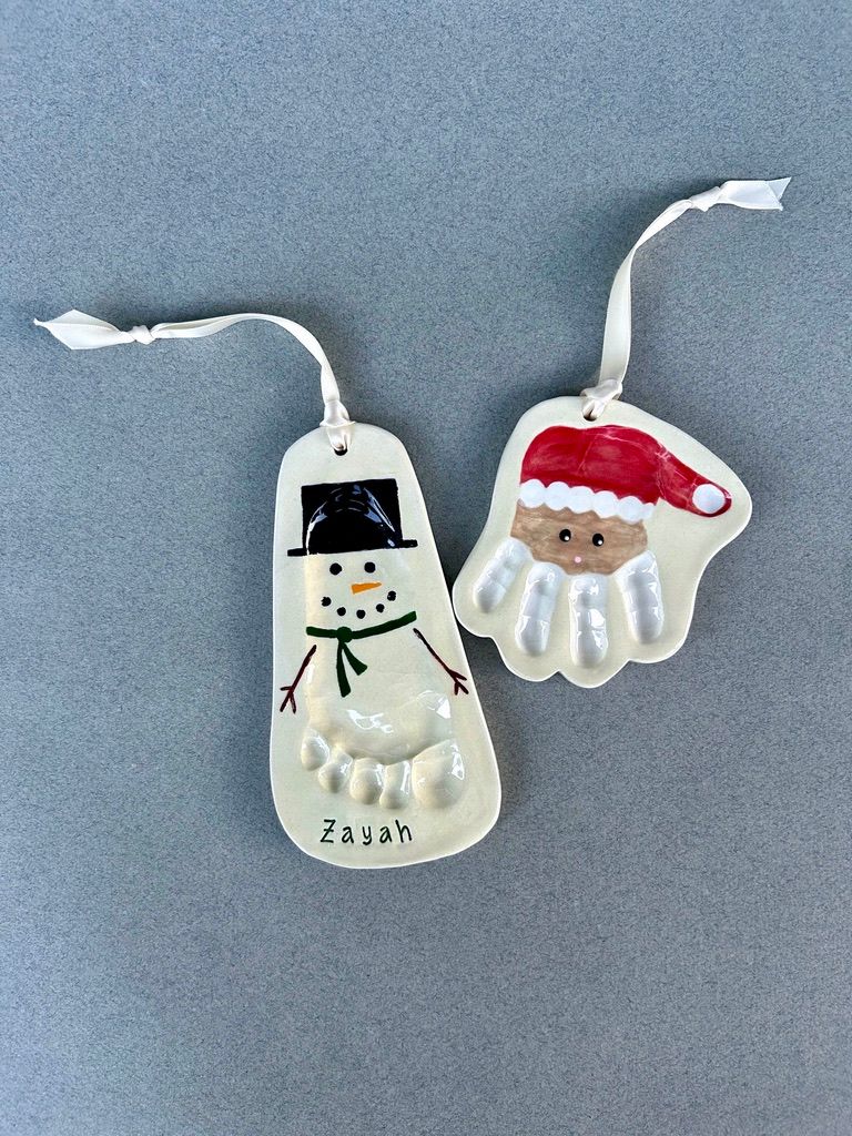 Footprint snowman and handprint Santa ceramic ornaments on a grey backdrop.
